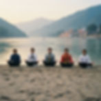 Five men in meditation pose on a sandy riverbank, wearing colorful and formal clothing. Hills and buildings are visible in the background. Calm mood.