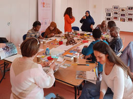 Women and people of different races and religions sitting around a table and participating in a collage and arts workshop