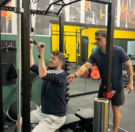 Personal trainer begeleidt klant tijdens lat pulldown krachttraining in fitnessruimte – Fitvers Fitness in Leuven en Aarschot.
