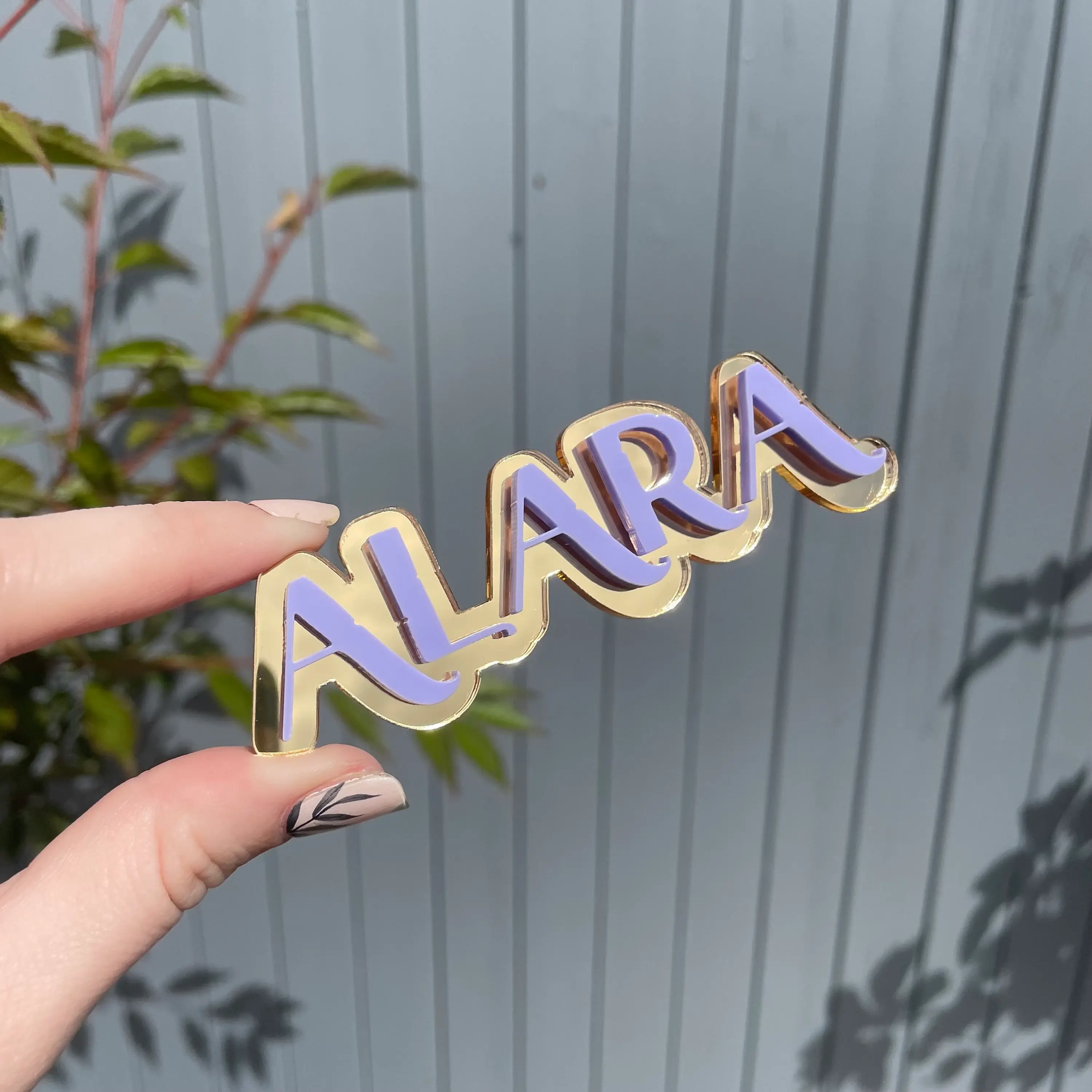 Hand holding a gold and purple ALARA name pin