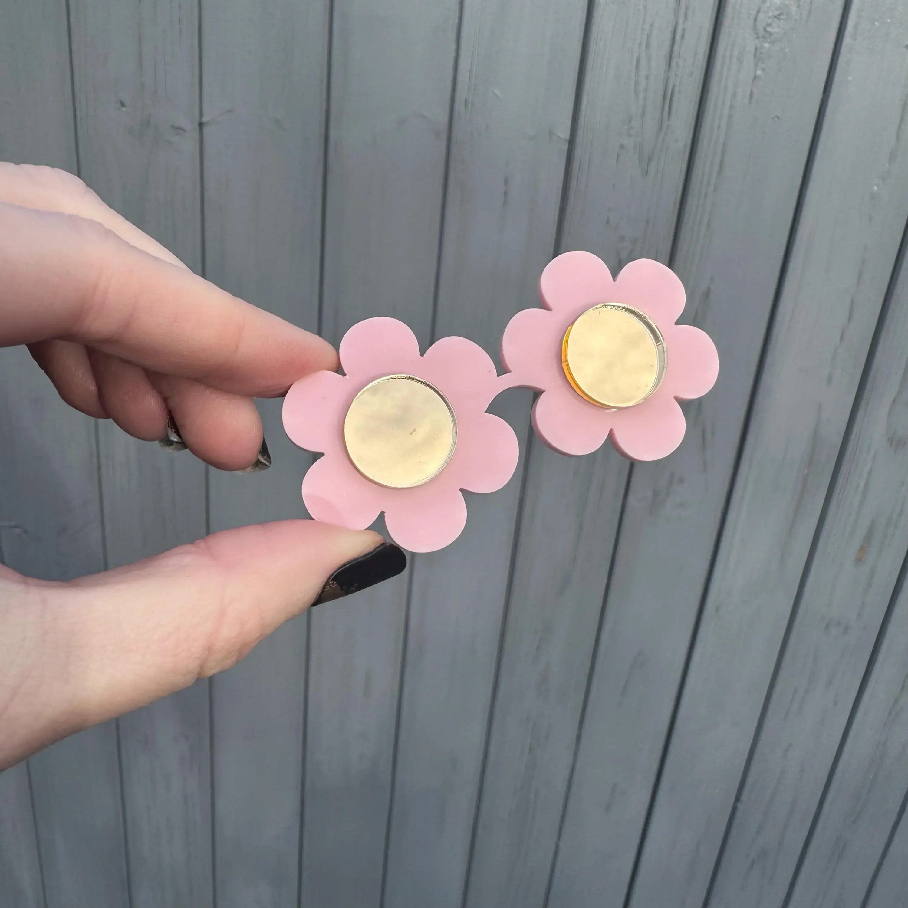 Hand holding two pink flower earrings with gold centers