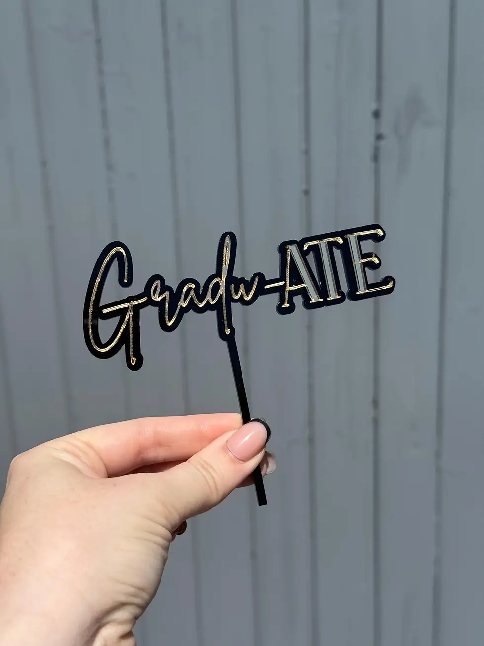 Thumbnail: Hand holding 'GRADUATE' cake topper
