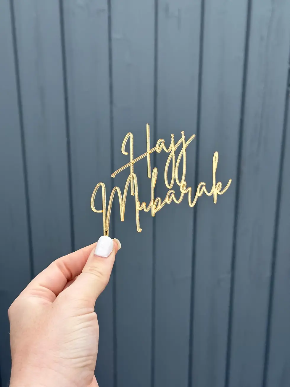 Hand holding a gold Hajj Mubarak cake topper