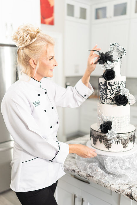 long body view of woman looking and touching black and white lace tiered cake with mask decor on top