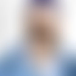 Siyah gözlük ve mor bere takan sakallı adam, mavi ceket giymiş. Parmağını yüzüne yakın tutuyor. Yüzük ve dövmesi dikkat çekiyor.