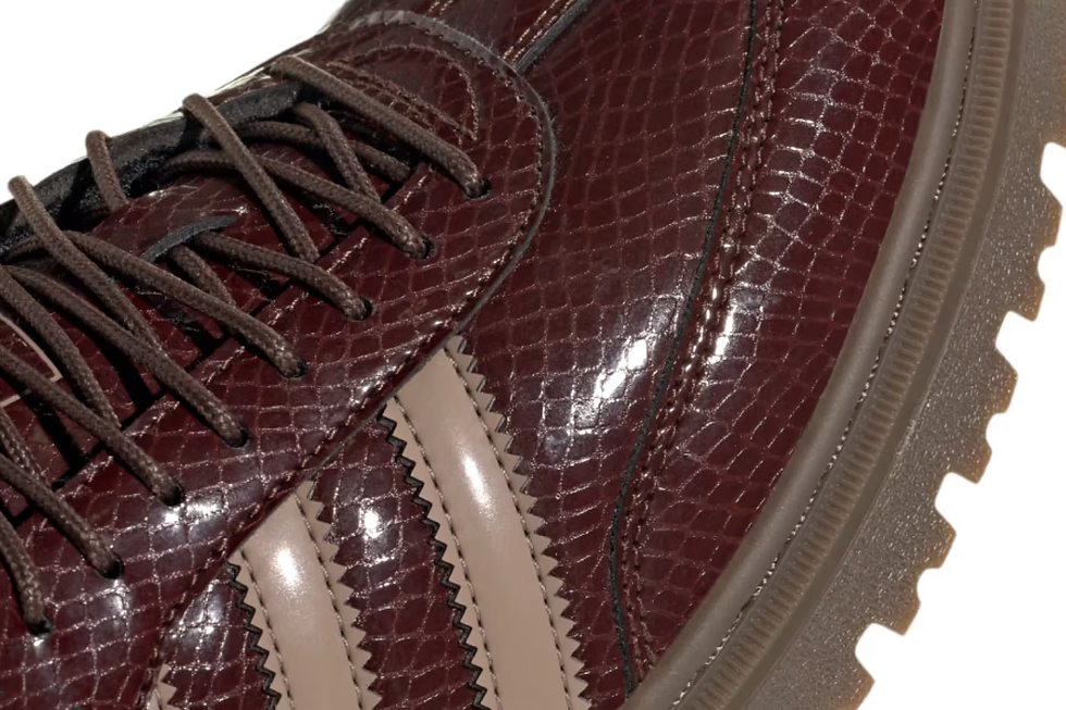 Kahverengi yılan derisi desenli bir spor ayakkabının yakından görünümü. Bej şeritler ve koyu bağcıklar detaylı. Arka plan beyaz.