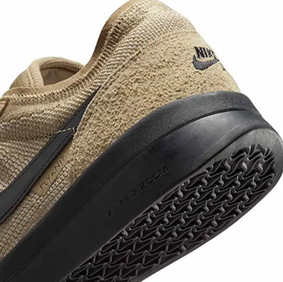 Bej Nike spor ayakkabının arka ve taban kısmı. Siyah Nike logosu, "FLYNIT" etiketi ve "AIR ZOOM" yazısı görülüyor. Taban siyah.