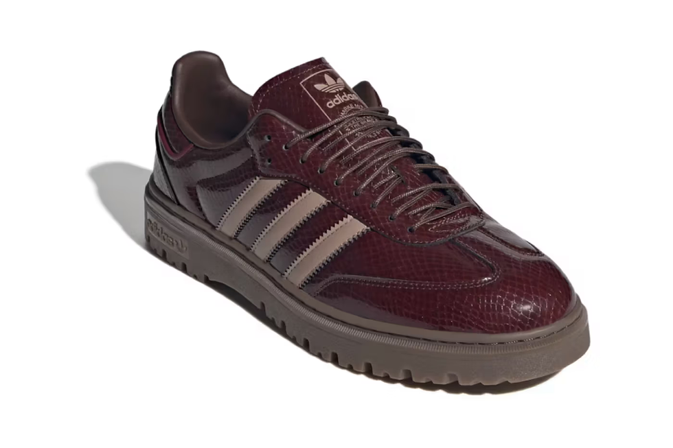 Kahverengi, deri görünümlü spor ayakkabı. Yanında üç beyaz çizgi var. Adidas logosu dil kısmında yer alıyor. Arka plan beyaz.