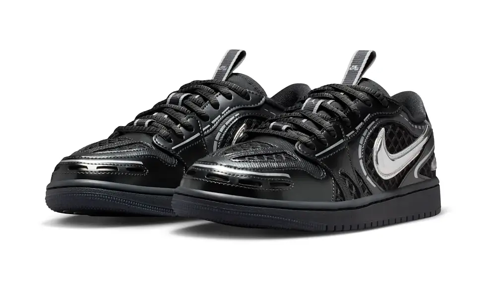 Siyah spor ayakkabılar, parlak ve desenli yüzeylere sahip. Gümüş renginde Nike logosu öne çıkıyor. Arka plan beyaz, sade bir ortamda.
