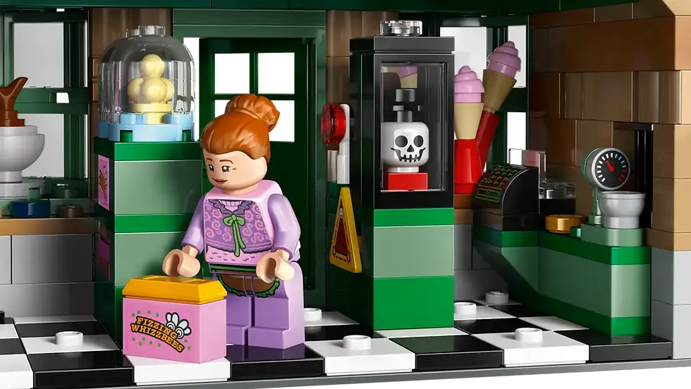 Lego figürü dondurmacıda. Üstü mor, sarı kutu tutuyor. Arkadaşı, dondurma makineleri, siyah-beyaz karo zemin ve kasa var.