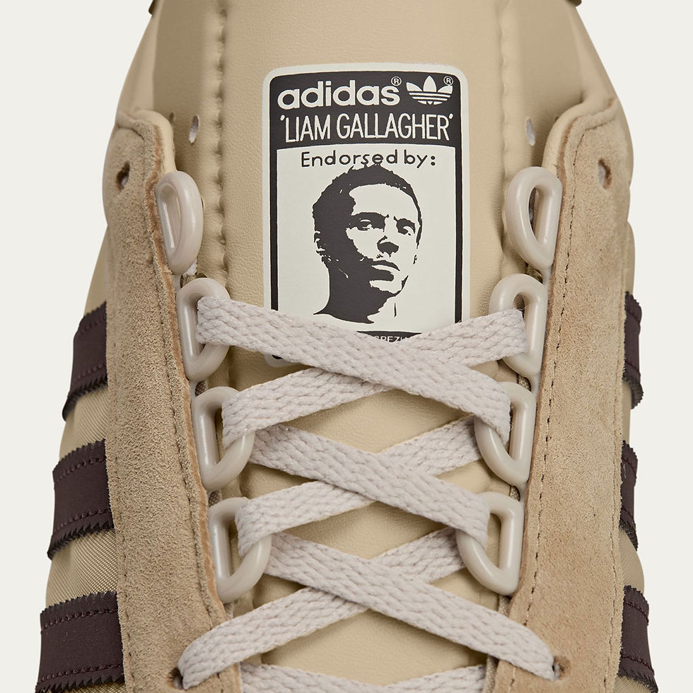 Bej ve kahverengi ayakkabı üzerinde beyaz bağcıklar var. Dil kısmında 'adidas', 'Liam Gallagher' ve 'Endorsed by' metni ve bir yüz resmi bulunuyor.