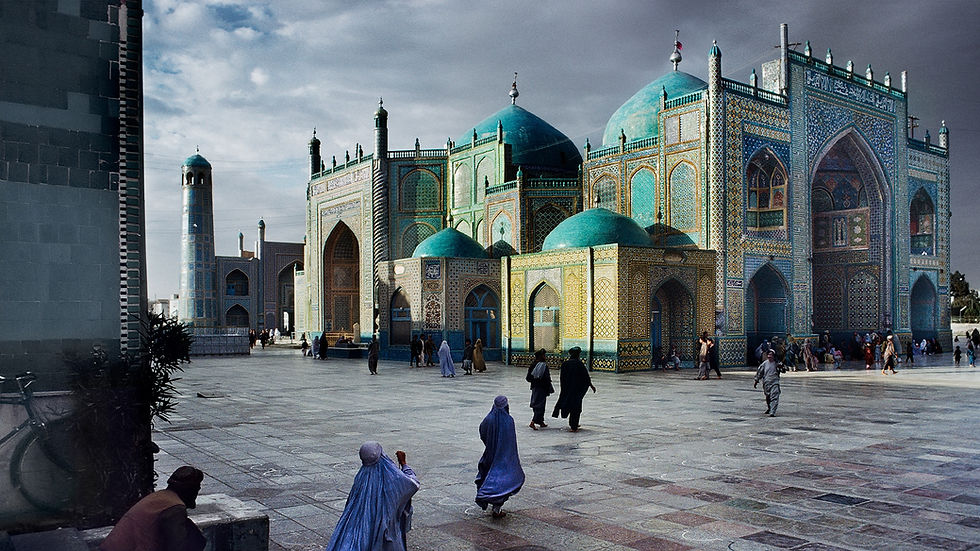 Mavi kubbeli cami avlusunda yürüyen insanlar. Çini desenli duvarlar, açık tonlu gökyüzü. Sakin ve huzurlu bir ortam.
