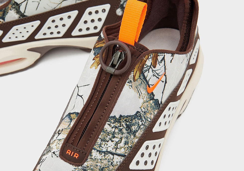 Kahverengi-yeşil desenli spor ayakkabı, turuncu Nike logosu ve fermuar detayları. Yan panelde "AIR" yazısı mevcut. Arka plan beyaz.