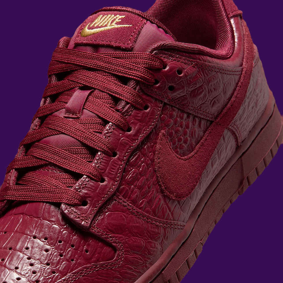 Bordo, timsah deri desenli Nike spor ayakkabı, mor arka plan üzerinde, altın Nike logosu ve bordo bağcıklarla dikkat çekiyor.