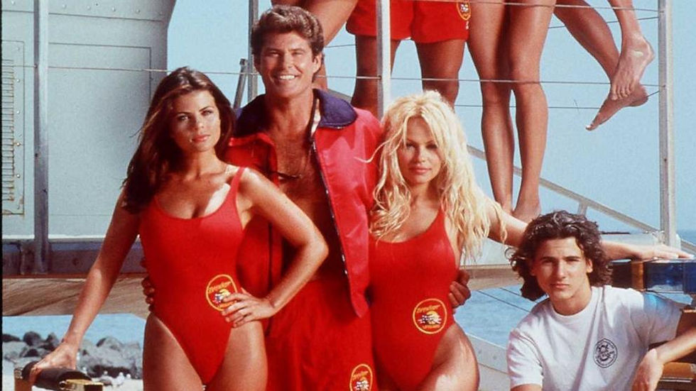 Kırmızı mayo giymiş dört kişi, arka planda deniz ve kule. Gülümseyen grup, enerjik ve neşeli. Üzerlerinde "Baywatch" logosu.