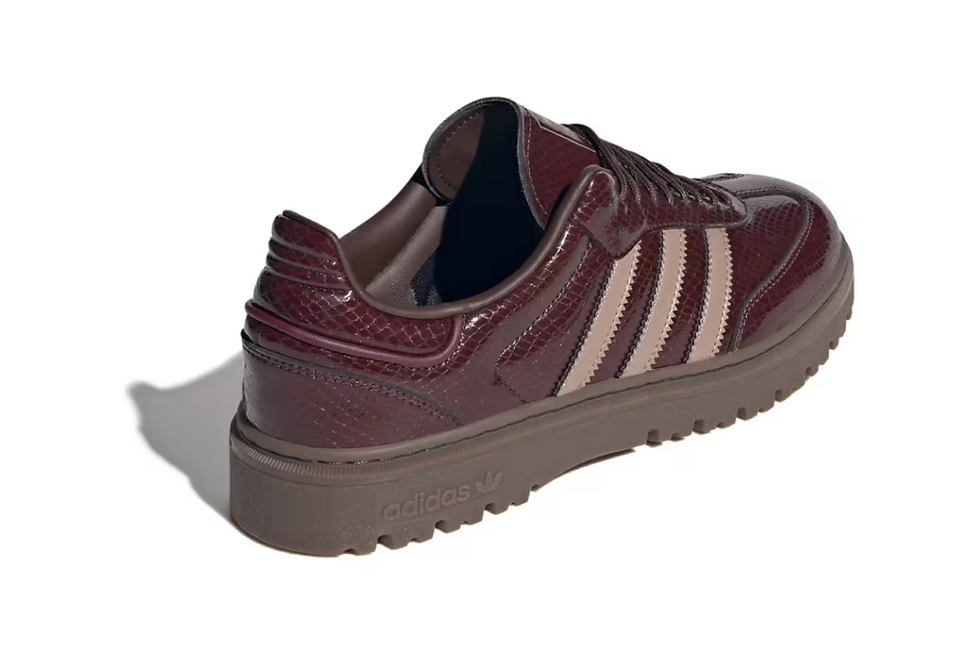 Kahverengi ve bej çizgili Adidas spor ayakkabı. Yılan derisi deseni var. Arka plan beyaz, ayakkabı şık bir tasarıma sahip.