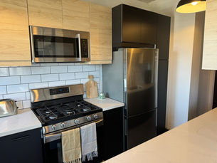 Modern kitchen with stainless steel appliances, including a fridge, oven, and microwave. Light wood cabinets, white subway tiles.