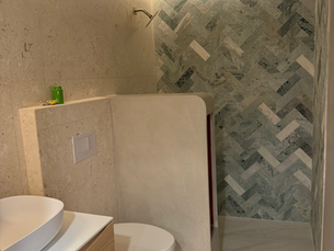 Modern minimalist bathroom with white sink and toilet, stone-tiled shower wall, and warm LED strip lighting.