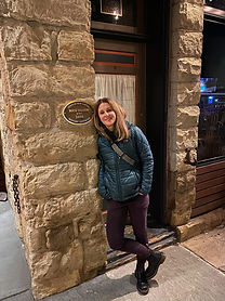 A young woman casually leans against a stone wall.