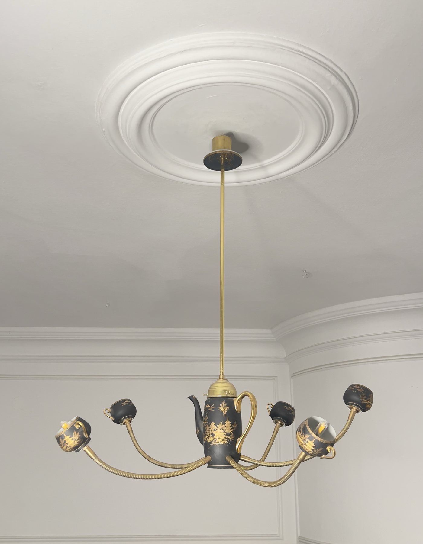 The Empress, switched off: a black and gold teapot and cups on curved brass arms, hanging from a ceiling rose