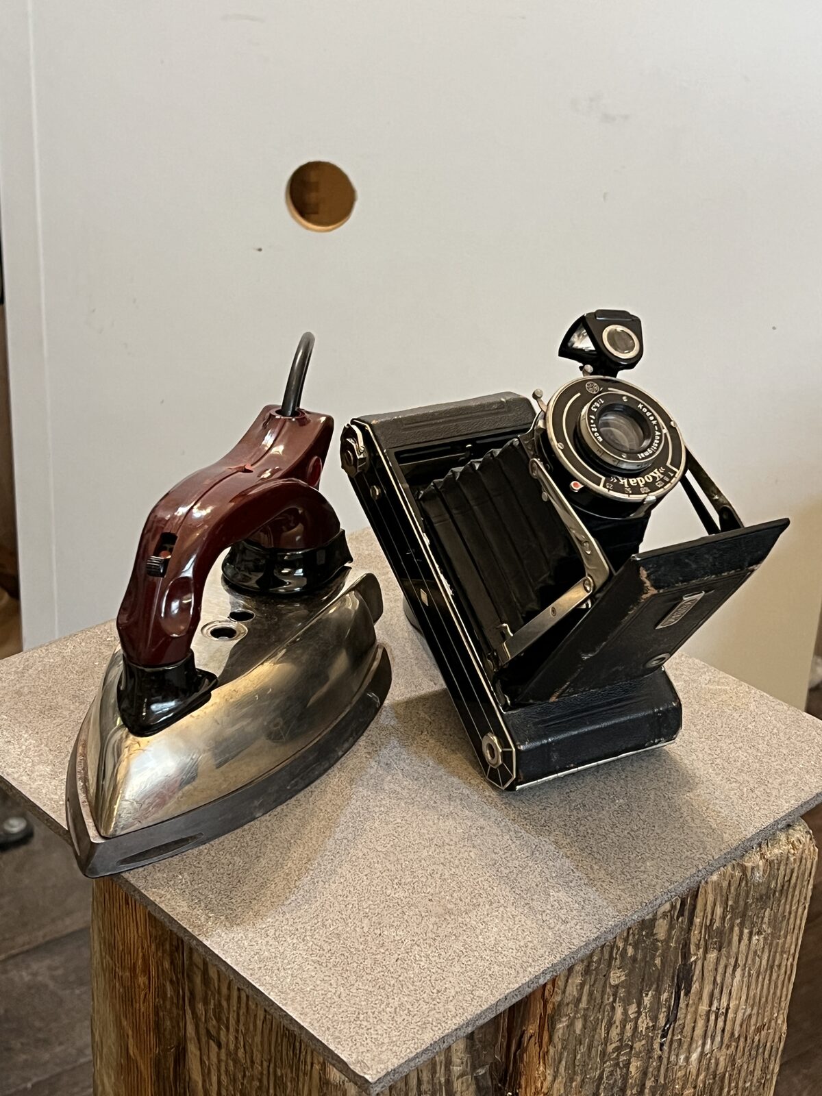 Iron Camera before: Flat iron and folding camera side by side on a wooden plinth