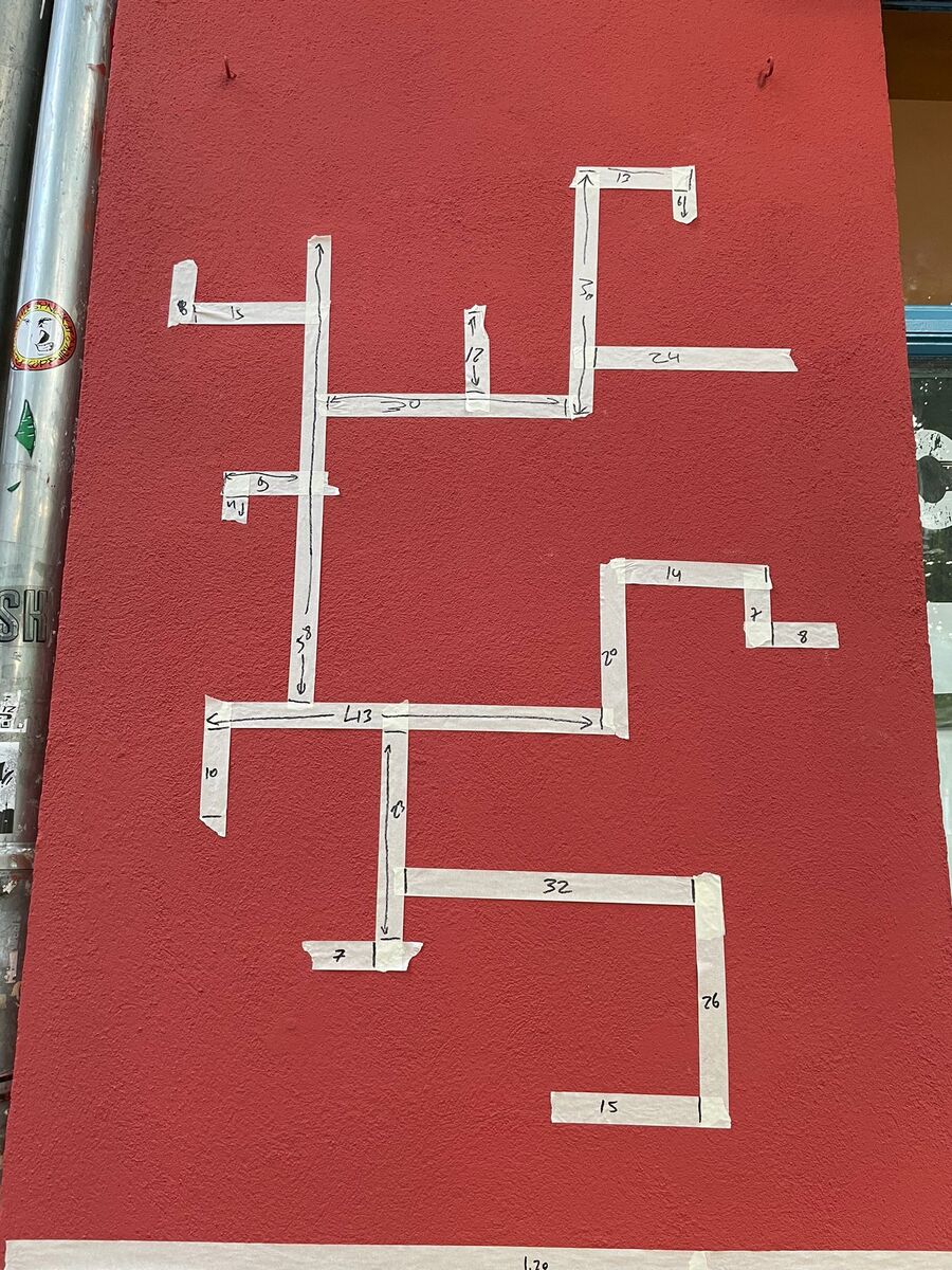 The maze laid out in masking tape on the red wall, each segment marked with its length