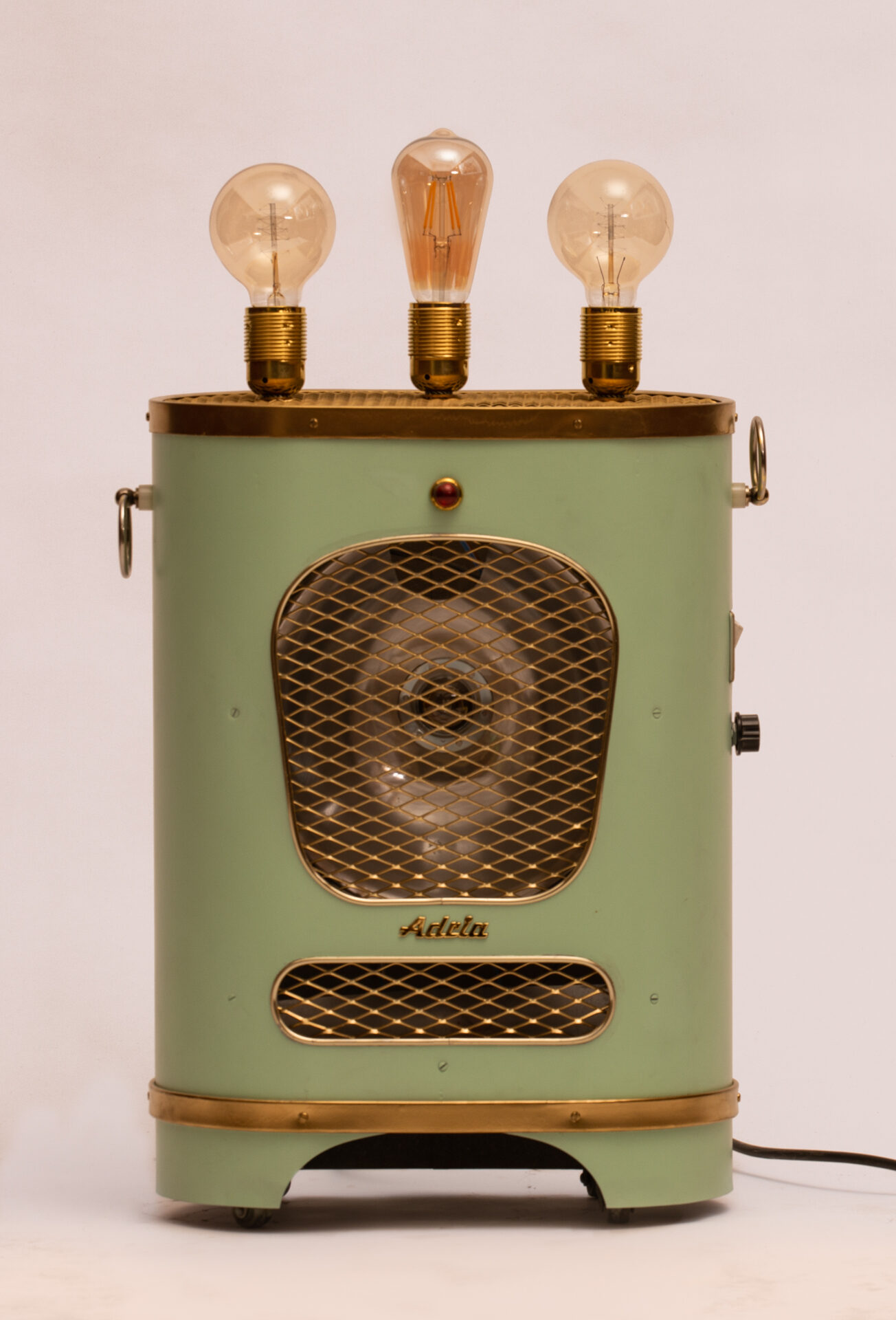 The Green Heater, switched off: a sage green 1950s heater with a chrome grille, brass trim and three Edison bulbs on top