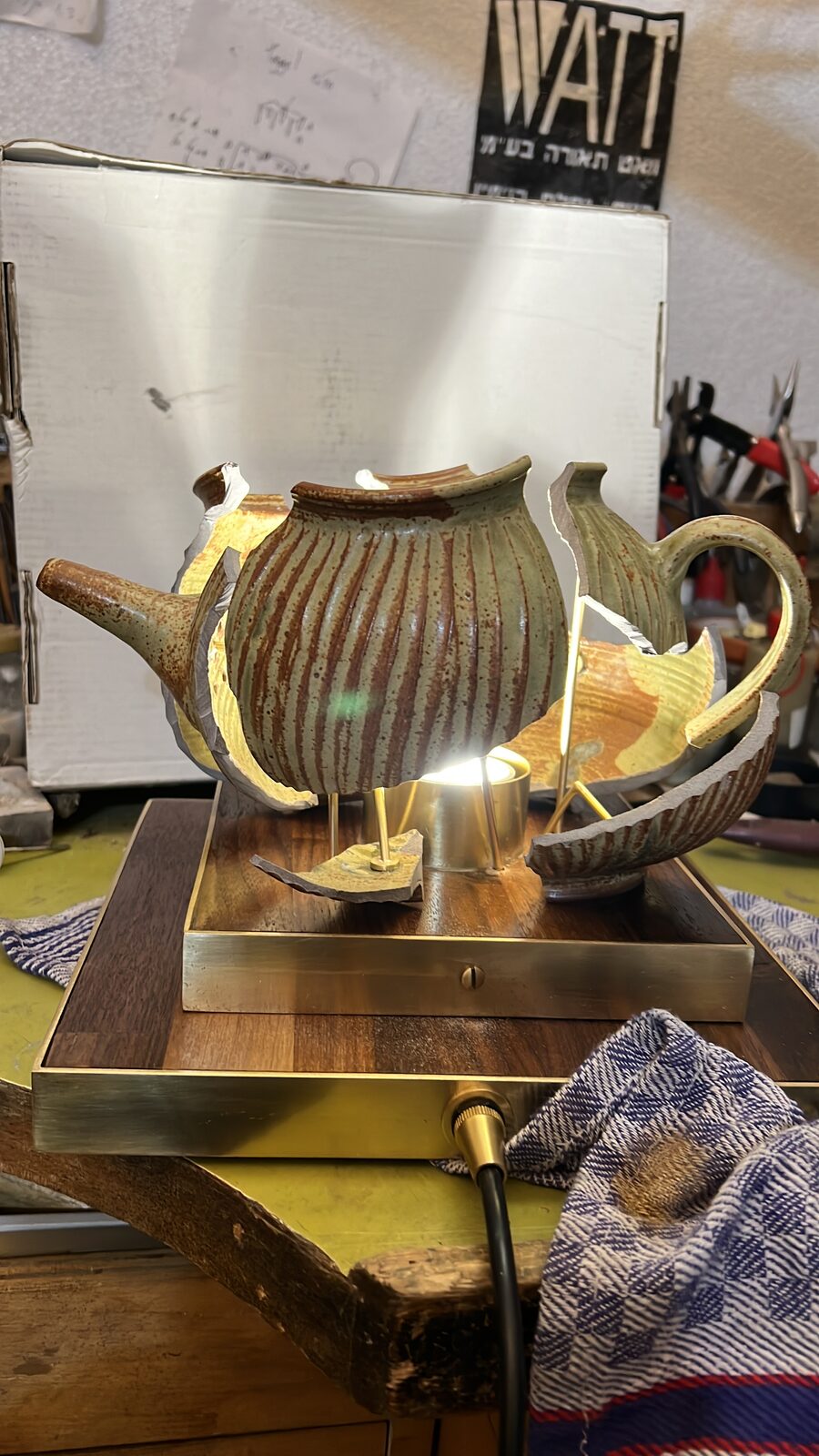 Ribbed teapot on its brass-edged base, WATT sign behind