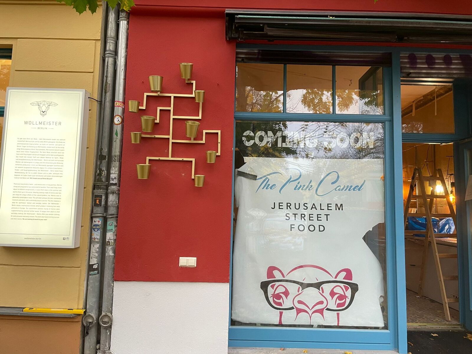 The Pink Camel's red front in Prenzlauer Berg before it opened, a brass maze with small brass plant cups on the wall beside the window
