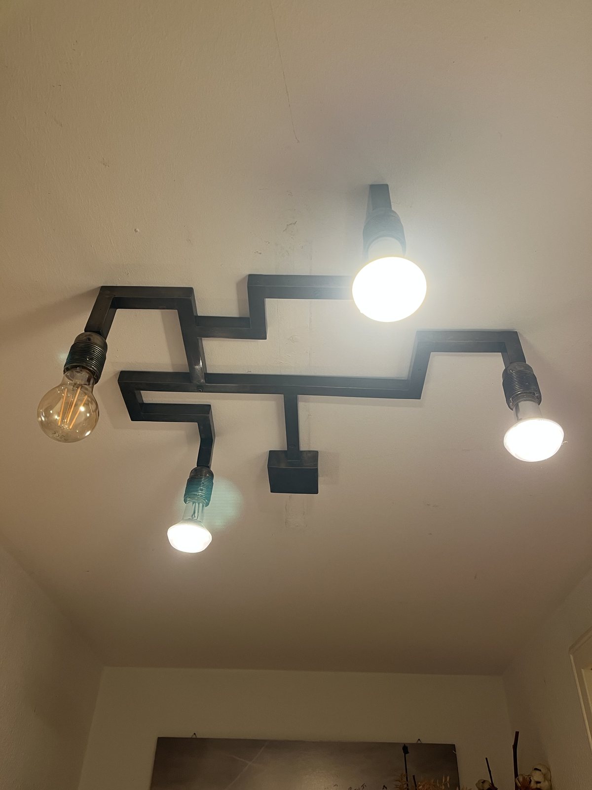 The brass lines reworked into a ceiling light for a hallway, its bulbs lit
