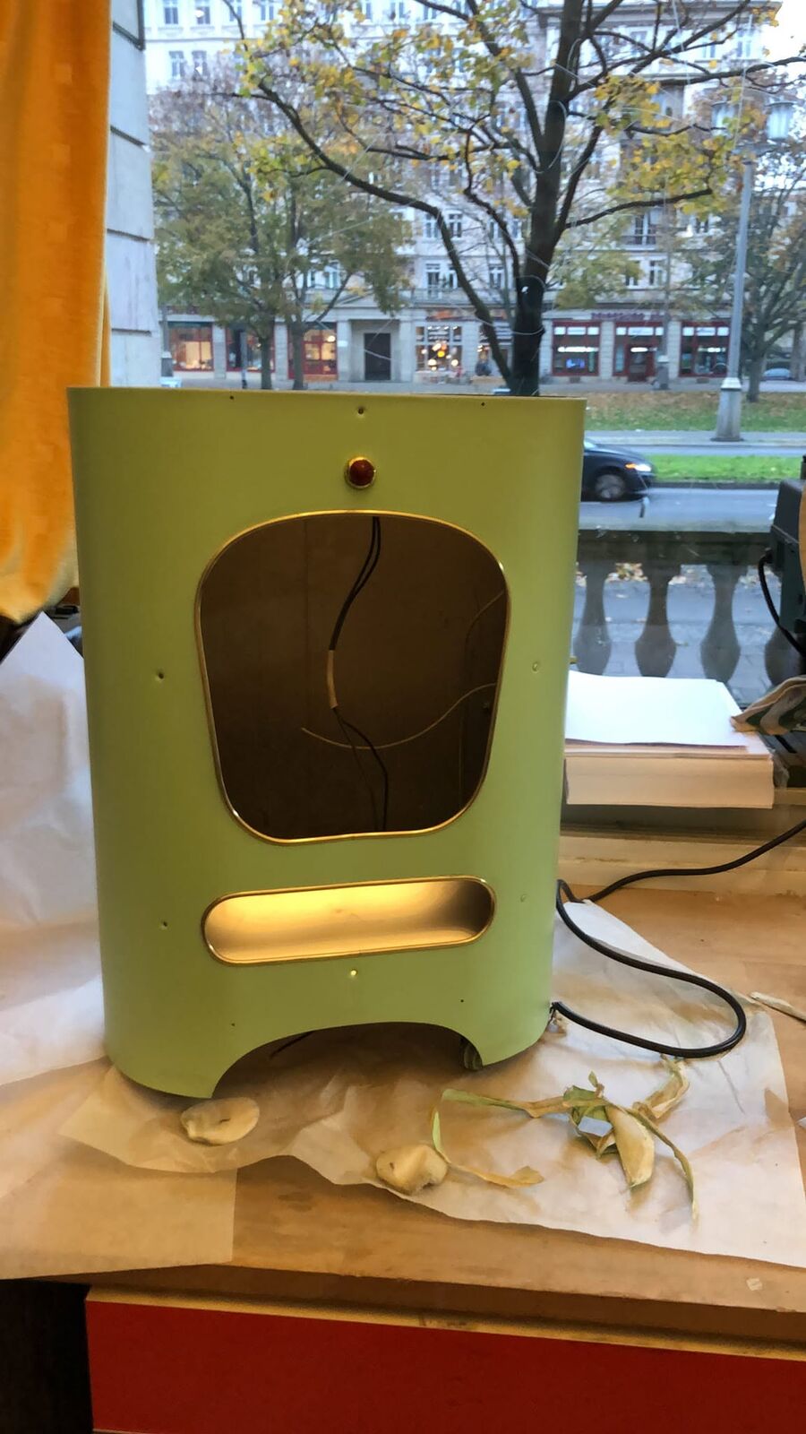 The green heater body by the studio window, grille out, light glowing inside, the street outside