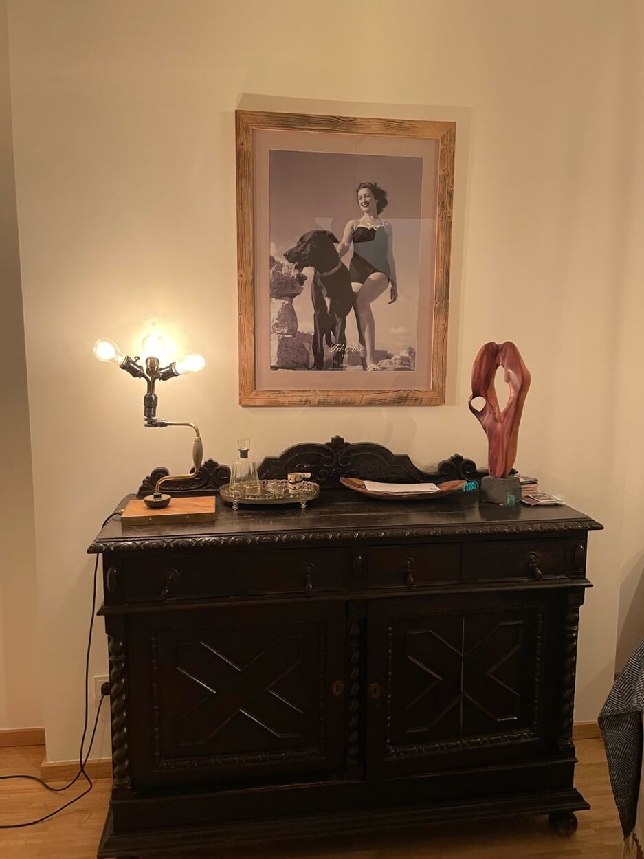 A hand drill made into a lamp with three bulbs, lit, on a dark sideboard