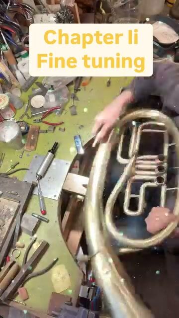 Hands working on the tuba's valves on a green bench full of tools