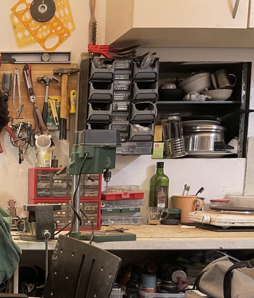 The tool wall in the studio: pliers and hammers on the pegboard, the drill press, boxes of parts