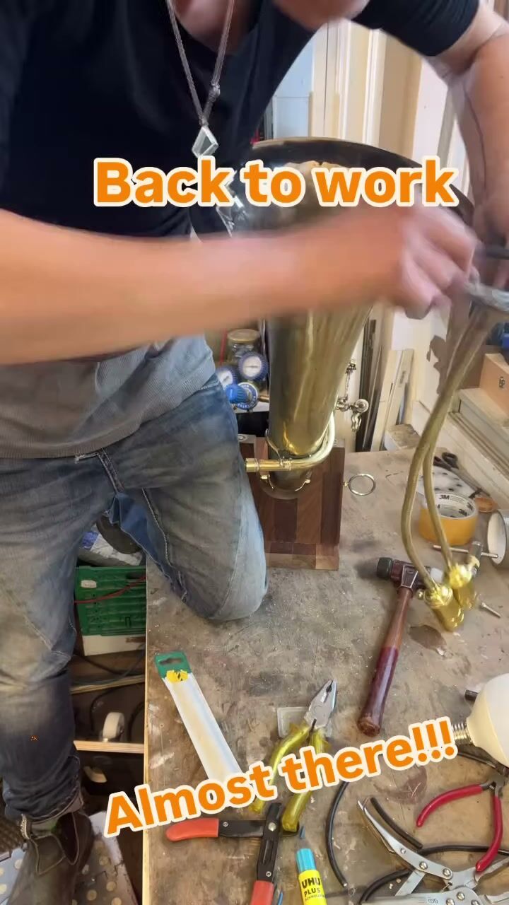 Keren kneeling at the bench, threading brass goosenecks into the tuba's bell
