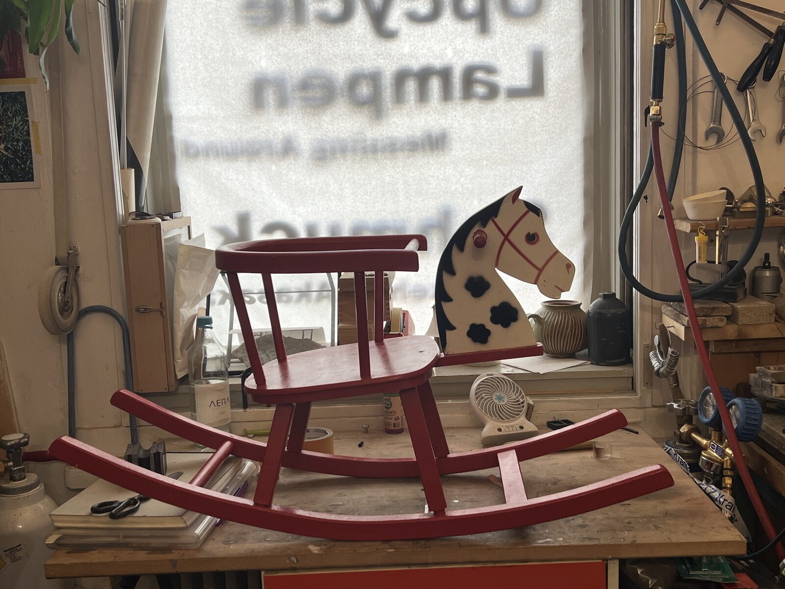 Horse Lamp before: Red child's rocking horse whole on the bench, shop window behind