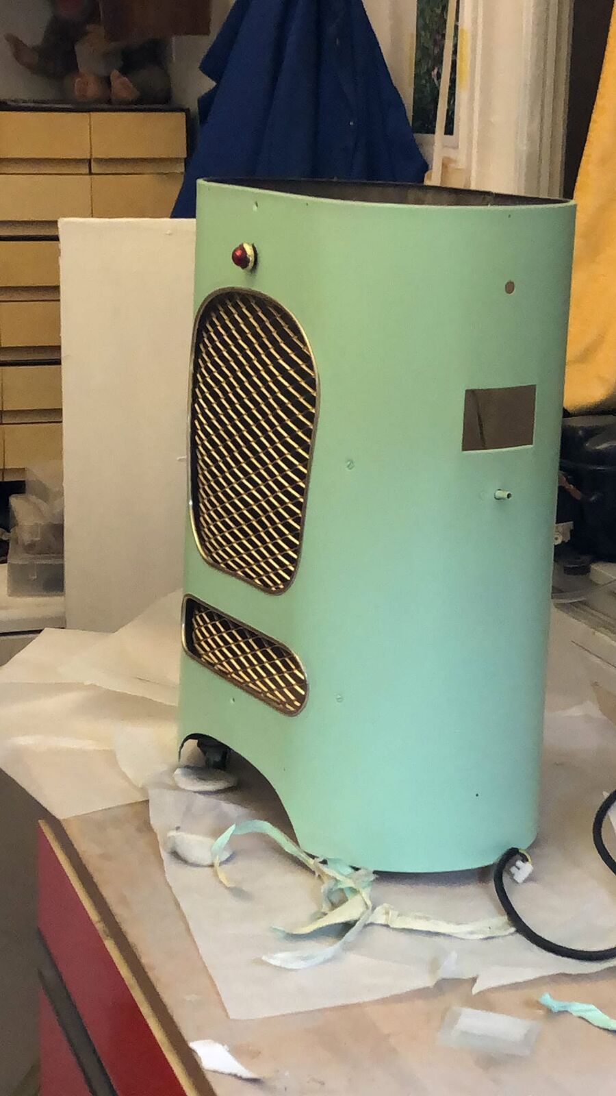 The heater body on the studio bench, painted a pale green, the grille still in place, tape and paper around it