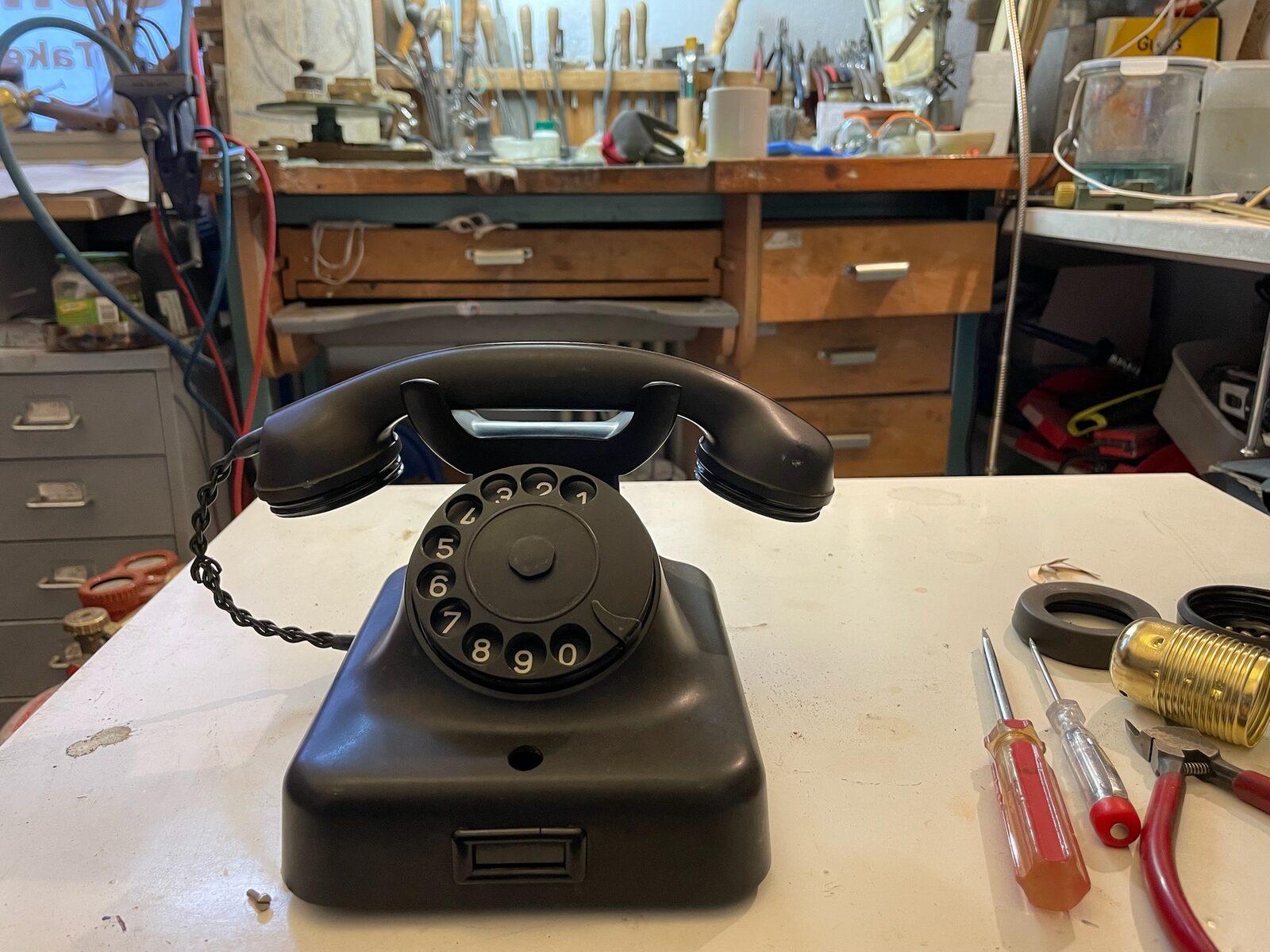 Black Phone before: Black rotary phone whole on the white bench, workshop behind