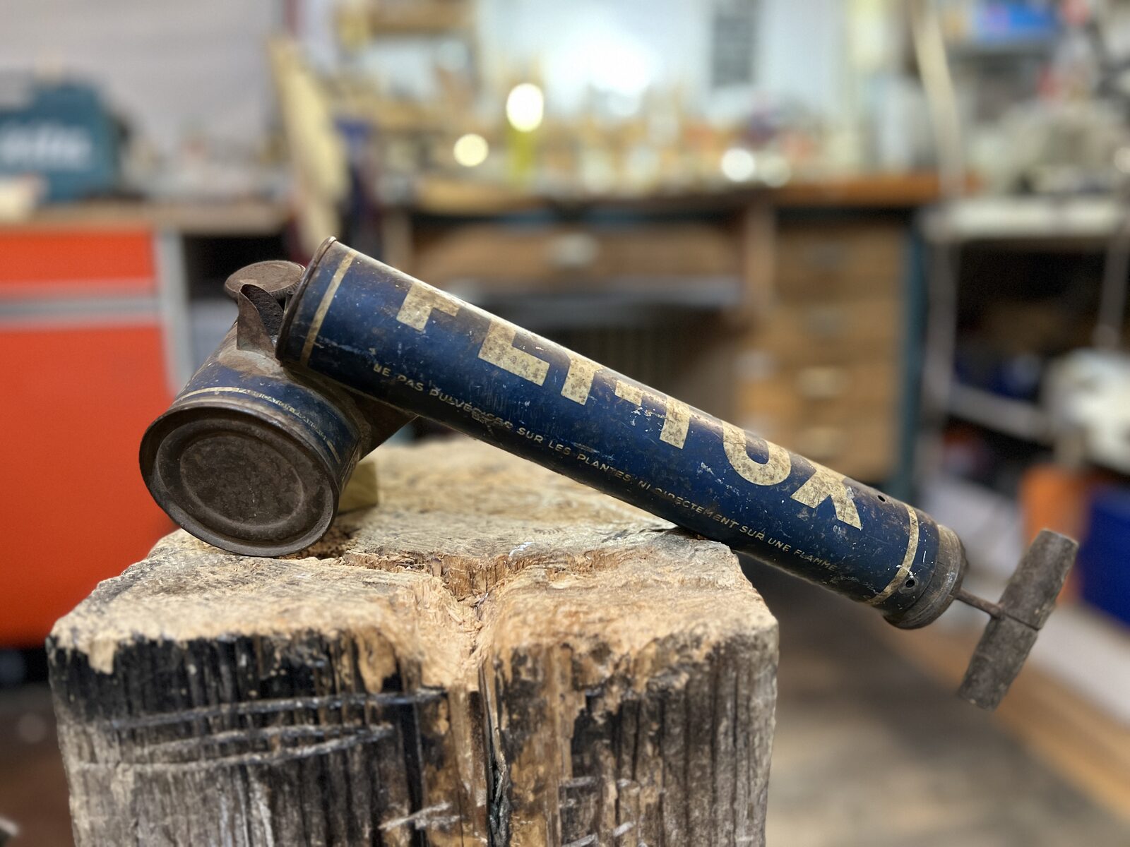 Flit Lamp before: FLITOX pump sprayer lying on a wooden stump in the workshop
