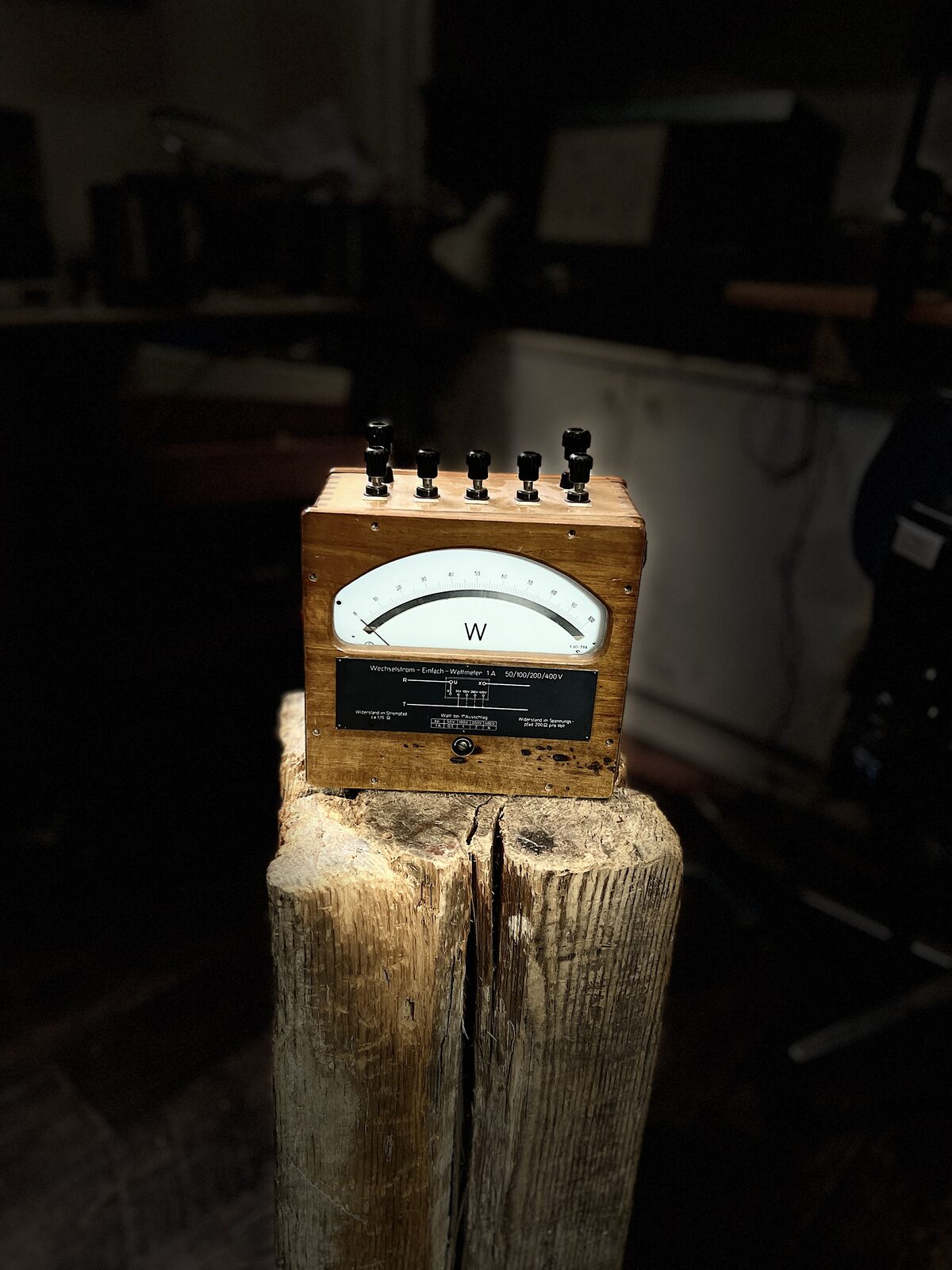 Watt Meter (Triangle) before: Wooden-cased watt meter on a stump in the dark workshop