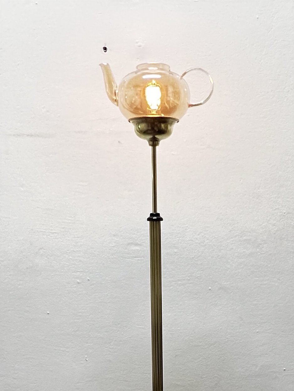 A standing lamp: a glass teapot with a bulb inside, on a tall brass column