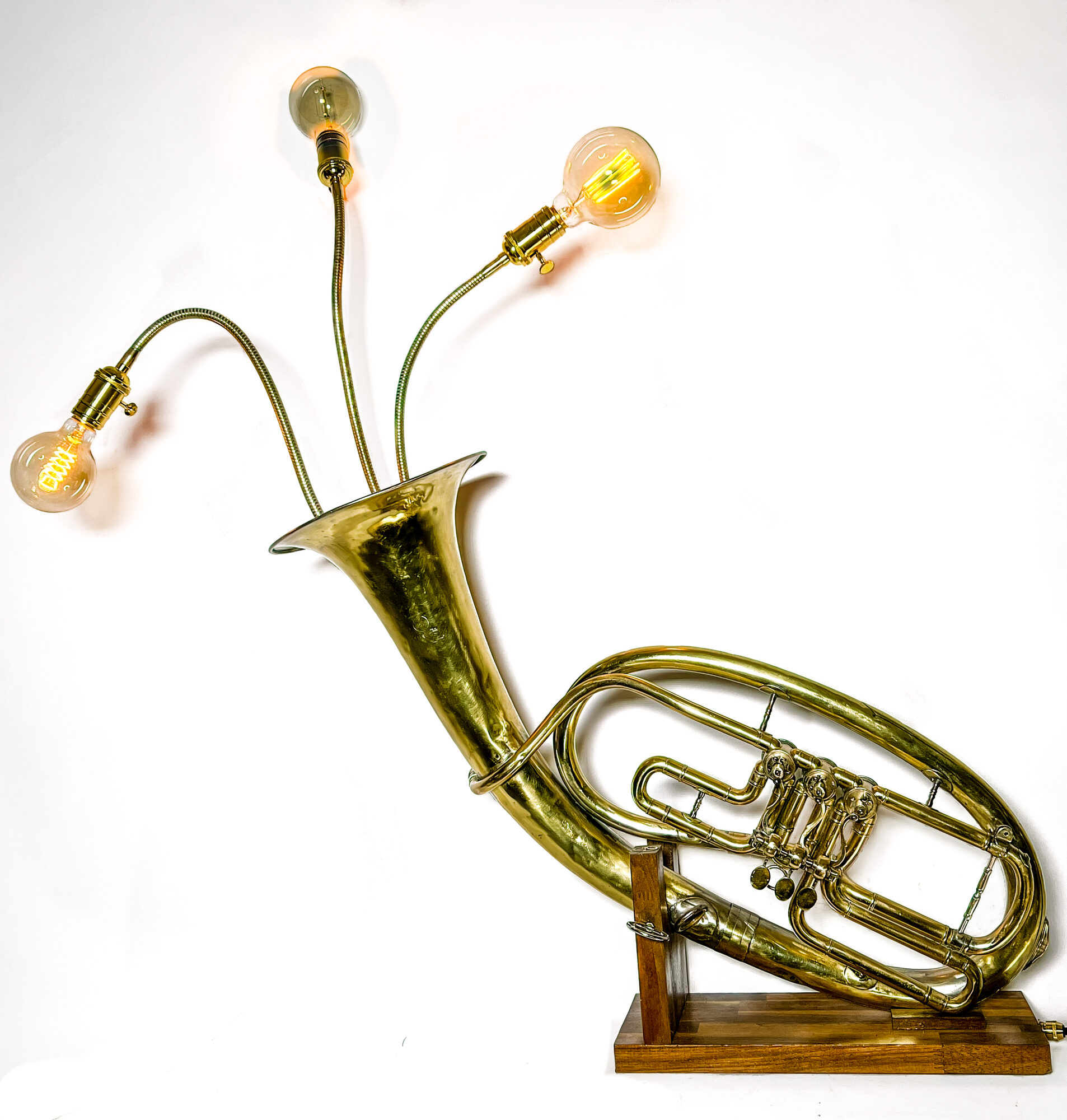 The Tuba lamp, lit: a brass tuba on a walnut base with brass gooseneck arms and Edison bulbs