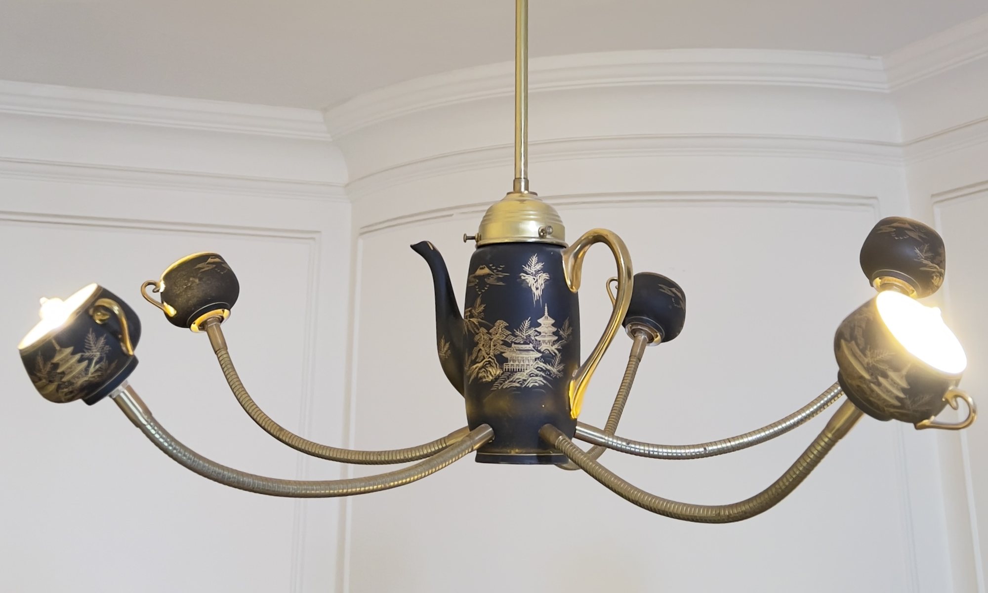 The Empress lit: a black and gold teapot and cups on curved brass arms