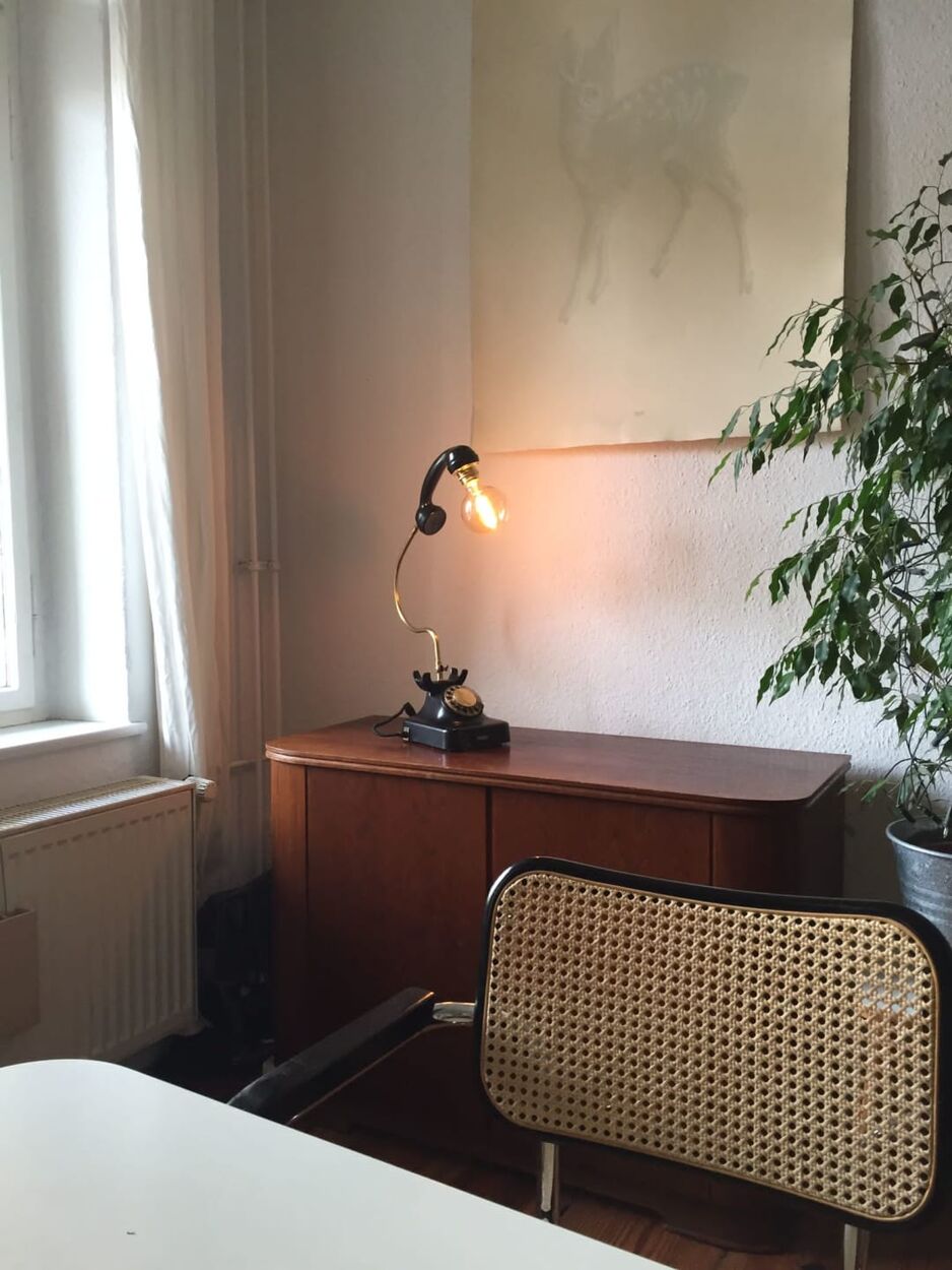 A black rotary telephone turned into a desk lamp, lit, on a wooden sideboard by a window