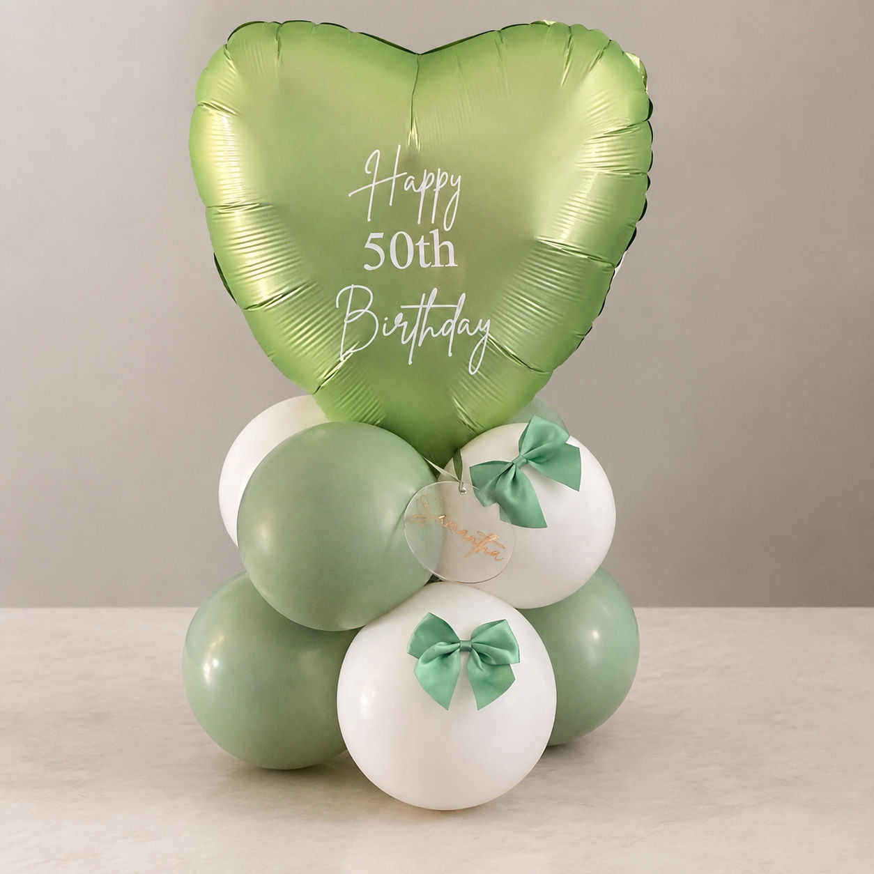 Personalised green heart foil birthday balloon tabletop display with sage and white latex balloons and matching bows.