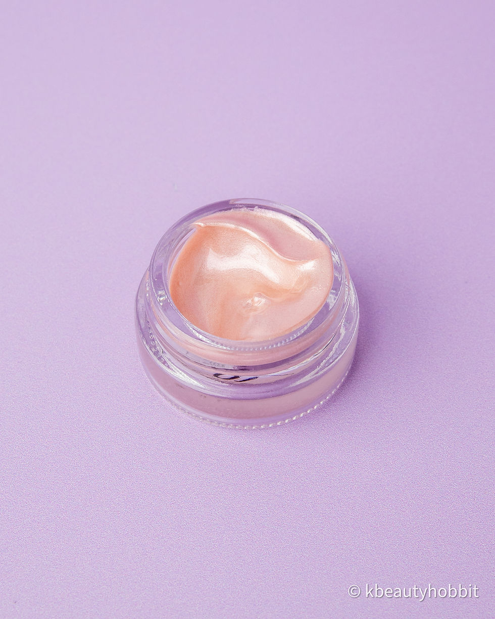 Small container of shimmering peach cream on a purple background, with minimal text visible on the container's edge.