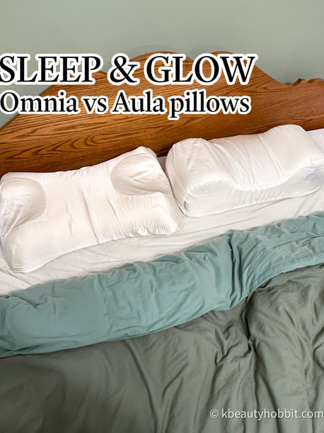White pillows on a wooden bed with teal bedding. Text reads "SLEEP & GLOW: Omnia vs Aula pillows." Calm, neutral setting.