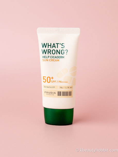 Sunscreen tube labeled "WHAT'S WRONG? HELP CICADERM SUN CREAM 50+ SPF/PA++++" on a pink background. Green cap, minimalist design.