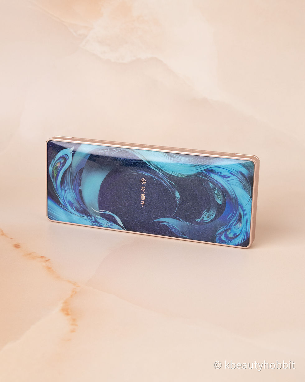 Makeup palette with swirling blue design on the lid, displayed on a beige marbled surface. Text in the center adds a stylish touch.