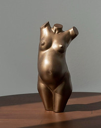 This is a resin sculpture of a nude, pregnant woman sitting on a wooden table. The woman’s body is curved and her arms are outstretched. The sculpture is made of resin and has a smooth, polished surface. The woman’s body is depicted in a natural, sensual way, with no details or ornamentation. The sculpture is designed to be a representation of the female form, with a focus on the curves and lines of the body. The sculpture is intended to be a decorative piece, and is suitable for placement in a home or office.